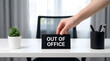 © Khan - A hand places an out of office sign on a white desk in a modern office environment