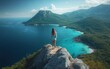 © zhuan - Woman standing barefoot on a rocky cliff overlooking a turquoise bay, lush green mountains and winding coastline under a clear sky, evoking awe and freedom