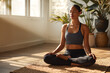 © EricMiguel - Mixed - race yoga practitioner meditating cross - legged, eyes closed, in dark gray sports bra, black leggings and gold necklaces in sunlit minimalist room