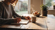 © NeuroCake - Woman writing in a journal at a wooden table with a cup of hot coffee. Female student or author taking notes in a notebook during a morning routine