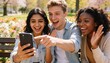 © Future Vision - Smiling three friends leaning toward smartphone on wooden park bench, floral beds and denim jacket