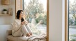 © Aldabra Studio - Asian woman relaxing with coffee by window in cozy home interior