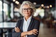 © nsit0108 - Professional woman with gray hair and glasses standing in a modern office looking at camera