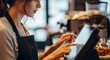 © Nazlykhan - Woman barista using touch screen pos system in coffee shop. Employee processing customer order on digital tablet. Small business management, retail technology, service worker concept.