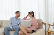 © Ratirat - Couple using laptop together on cozy sofa at home, browsing internet, online shopping.