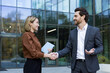 © Liubomir - Two smiling business professionals are shaking hands, confirming a successful agreement and partnership outside a modern office building, symbolizing deal closing and collaboration