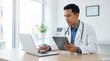 © Illustratorstock - A male doctor, wearing a white coat and stethoscope, sits at a desk in a bright clinic. He uses both a laptop and a tablet, reviewing patient data with a focused, professional expression.