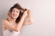 © New Africa - Unhappy woman trying to brush her tangled hair on light grey background, space for text