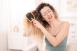 © New Africa - Unhappy woman trying to brush her tangled hair at home, space for text