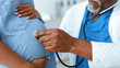 © Prostock-studio - A doctor uses a stethoscope to listen to the heartbeat of a pregnant woman in a medical office. The woman rests her hand on her belly as part of a routine check-up.