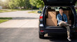© Olesya - Graduate man sitting in back of car with cardboard boxes. Young student move out concept. High school or college commencement. Education transition and independence in life. New beginning.