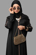 © Pixel-Shot - Beautiful young stylish Muslim woman in black hijab with golden accessories and sunglasses on grey background