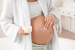 © Pixel-Shot - Young pregnant woman applying cream on her tummy in bathroom, closeup