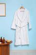 © Pixel-Shot - White bathrobe hanging on blue wall and different bath supplies on table in bathroom