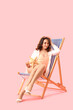© Pixel-Shot - Young woman with starfish in deck chair on pink background