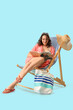 © Pixel-Shot - Young woman reading magazine in deck chair on blue background