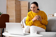 © Pixel-Shot - Young woman with cup of coffee video chatting on sofa at home