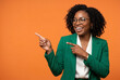 © Meow Creations - Smiling business woman in a green blazer pointing aside against a bright orange studio wall