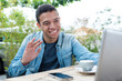 © auremar - young fashionable man sitting in cafe with laptop waving