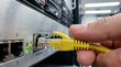 © Yauhen - Hand plugging yellow ethernet cable into server rack port. Represents network maintenance and data center connectivity. Useful for IT support and technology concepts.