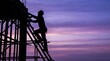 © 5 Grace Media - Silhouette of a construction worker climbing scaffolding against a vibrant sunset sky.