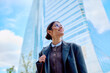 © we.bond.creations - Happy businesswoman wearing glasses looking up, standing in front of office architecture. Confidence and success in business