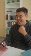 © Krakenimages.com - Man holding smartphone and making a fist pump gesture while seated at a study desk near books and bookshelf in a library building; joy celebration.