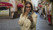 © Krakenimages.com - Woman covers mouth with hand while holding smartphone on a busy pedestrian street wearing glasses and patterned blouse; delight celebration.