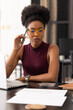 © wavebreak3 - African woman in yellow glasses working at home holding green pencil while reviewing papers