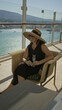© Krakenimages.com - Woman smiling in wicker chair holding champagne glass and touching sunglasses while wearing wide sunhat on building terrace by the sea; relaxation.