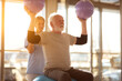 © Crowded Studio - Sesión de rehabilitación para adultos mayores con equipamiento de entrenamiento funcional. Un adulto mayor levanta pequeñas pelotas de ejercicio bajo la guía de un especialista en una sala luminosa