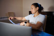 © Taras Grebinets - Woman Working Late in Home Office Sorting Documents at Desk With Laptop
