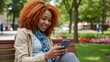 © Alexander Chaykin - Happy redhead sitting in park, engaging with digital device.