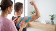 © Jai Izzam - Side view of therapist examining athlete shoulder with blue kinesiology tape in modern clinic