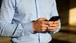 © Morgan - Man in blue shirt using smartphone closeup of hands typing on mobile phone modern technology concept digital communication business casual attire outdoor lighting professional