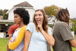 © Wavebreak Media - Diverse friends posing back-to-back on front lawn at gathering, woman touching face with sunglasses