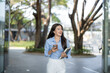 © Apichat - Asian woman walking, holding book and smartphone