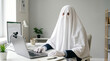 © solom - person dressed in white ghost sheet costume working on laptop at office desk funny concept for invisible employee ghosting at work burnout or halloween corporate celebration
