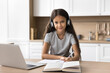 © fizkes - Portrait of cute little 7s schoolgirl studying at home using laptop, wear headphones listening audio course, improve english knowledge via application or educational platform. Modern tech, e-learning