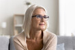 © fizkes - Beautiful pensive middle-aged woman wear glasses sit alone on couch and looking into distance with thoughtful, reflective expression, deep in thoughts, nostalgic mood, recollects, memories, close up