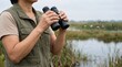 © Таня Андреева - Senior woman birdwatching with binoculars in a scenic marshland nature reserve.