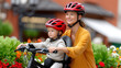 ©  VladaToday - Mother and child riding bike with helmets on park path for family outdoor activity and summer leisure banner