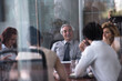 © .shock - Senior executive leading a business meeting in a modern glass boardroom with attentive team members