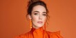 © DSimage - Elegant young woman in orange outfit and earrings posing against orange studio background