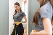 © KMPZZZ - Weight lose, loss concept. Slim body asian young woman hand use tape measuring around waistline in fit sports. Girl looking reflect in mirror at home. Healthy nutrition, fitness for wellbeing beauty.