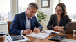 © Владлена Демидова - Businessman signing documents while sitting with colleague in office