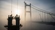 © DenS - Construction of a majestic suspension bridge shrouded in atmospheric fog during sunrise, with diligent workers on the towering structure