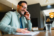 © djile - Happy businessman talking on phone while working remotely in cafe
