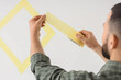 © Pixel-Shot - Young man applying masking tape to white wall at home, closeup