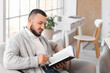 © Pixel-Shot - Handsome young man reading book on armchair at home
